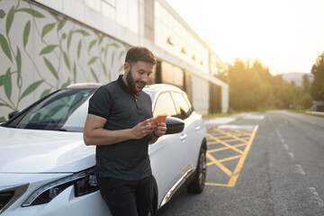 Man using phone supported on parked car