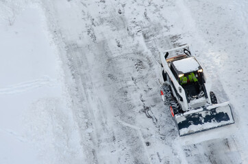 Skid steer loader removes snow from the city streets. Top view of the road with cars and snow...