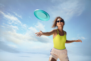 Happy African American woman throwing flying disk against blue sky on sunny day