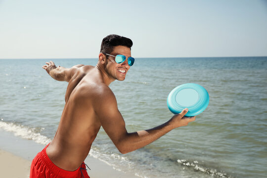 Happy man throwing flying disk at beach on sunny day