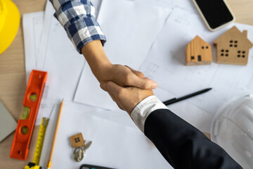 A construction team leader shakes hands with a home builder after agreeing a contract to work...