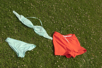 Women blue swimsuit and men's  red swimming trunks on the grass.