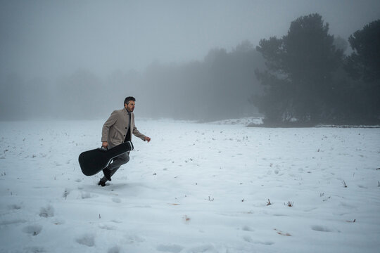 Mature man with guitar case running on snow