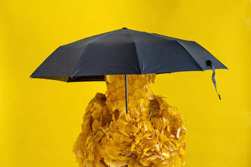 Woman wearing autumn leaf costume holding umbrella in front of yellow background
