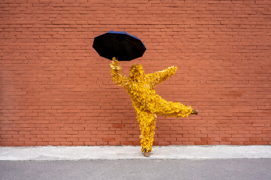 Woman with leaf costume holding umbrella while dancing by brick wall