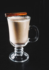 traditional Christmas drink Eggnog with cinnamon, anise, vanilla sticks on rustic wooden table on dark background