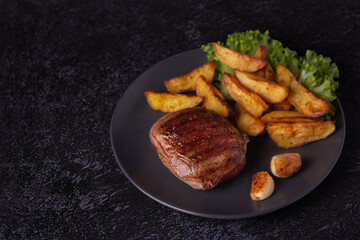 Photo of grilled marbled beef steak with potatoes and garlic on black
