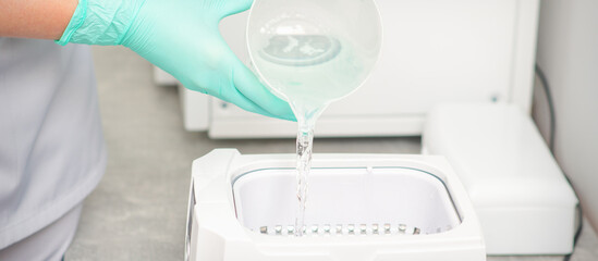 The beautician adds liquid for disinfection of instruments to the machine for sterilization of tools
