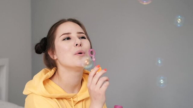 young woman girl in yellow making soap bubbles on grey background. happy, exited. slow motion.