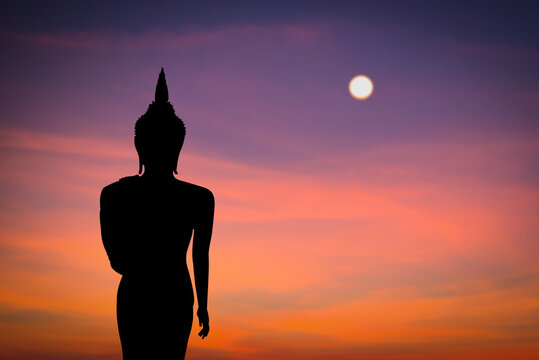 Silhouette of buddha with the sun over the sky at sunset background.