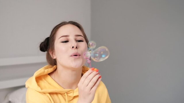 young woman girl in yellow making soap bubbles on grey background. happy, exited. slow motion.