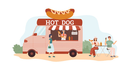 Young hipster couple sit at the outdoor cafe and eat hot dogs.Female cook sausages and sell them at street food truck