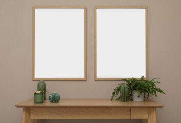 Empty frames hanging on beige wall over wooden table with decor. Mockup for design