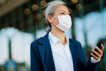 Grey asian woman in face mask using cellphone on airport parking