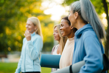 Multiracial women talking and smiling after yoga practice in park
