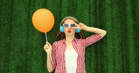 Portrait of happy young woman listening to music in headphones with orange balloon lying on the...
