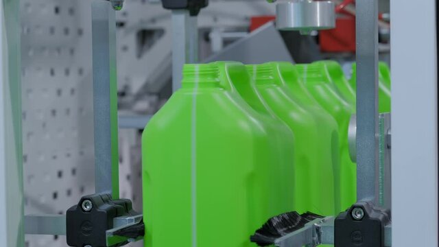Empty green plastic jerrycans falling from conveyor belt of automatic pet blow molding machine at factory, exhibition: close up. Manufacturing, recycling, automated technology equipment concept