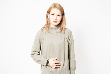 お腹を手で抑えるセーターを着た若い女性