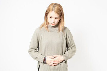 お腹を手で抑えるセーターを着た若い女性