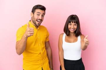 Young couple isolated on pink background giving a thumbs up gesture because something good has happened