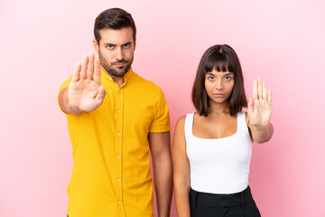 Young couple isolated on pink background making stop gesture denying a situation that thinks wrong