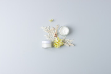 Jars of cosmetic cream with flowers on grey background. Flat lay, copy space