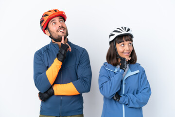 Young cyclist couple isolated on white background thinking an idea while looking up