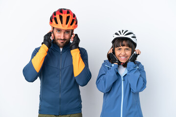 Young cyclist couple isolated on white background covering both ears with hands