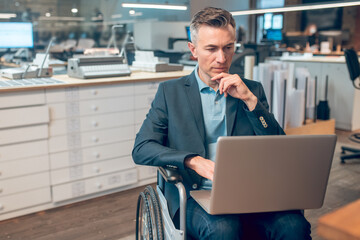 Man in wheelchair thinking working on laptop