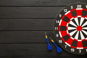 Dart board with red darts on black wooden background.