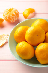 Fresh mandarin oranges fruit on mint bowl on pink wooden background. Vertical photo.