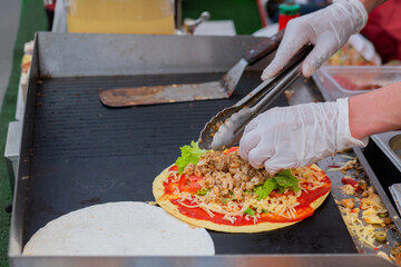 Chef preparing fresh quesadilla on black grill at summer local food market - close up view. Outdoor cooking, barbecue, gastronomy, cookery, street food and traditional Mexican dish concept