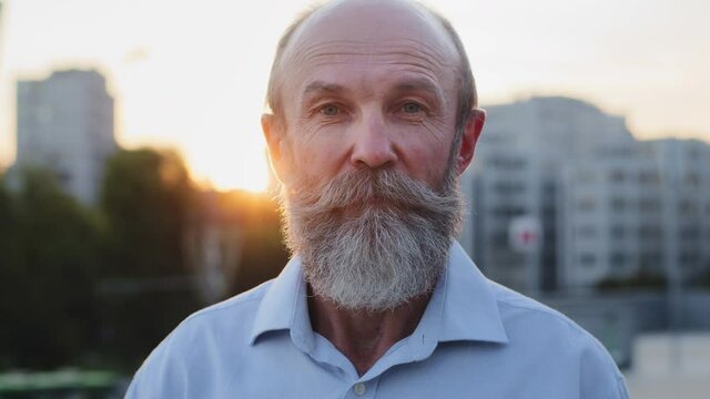 Handsome old grandfather with gray beard smiles affably, agree nods head, looking at camera. Satisfied elderly client, man of retirement age, confirms quality of service, pension insurance, agrees