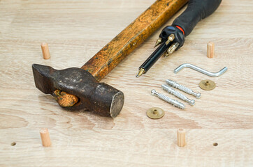 Hammer, screwdriver and fasteners on a wooden table. tools and parts for assembling cabinet furniture on a wooden surface from a chipboard sheet.