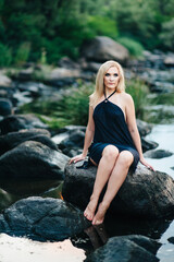 blonde girl in a black dress with blue eyes on the coast of the river