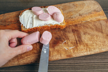  Cooking a sandwich. The hand cuts the sausage. Wooden cutting board. Bread with sauce and sausages.