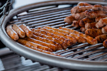 Process of grilling fresh meat sausages on big round hanging grill at summer local food market: close up view. Outdoor cooking, barbecue, gastronomy, cookery, street food concept