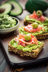 Guacamole dip or spread with open sandwiches and ham on wooden kitchen table