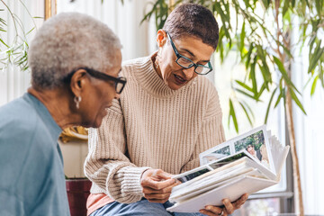 Mature woman shows a photo album to an elderly black woman at home