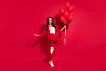 Fototapeta na wymiar Full body photo of impressed brunette lady hold balloons wear suit cap footwear isolated on red color background