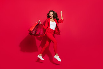 Full size profile photo of hooray brunette lady jump with bags wear suit sneakers isolated on red color background