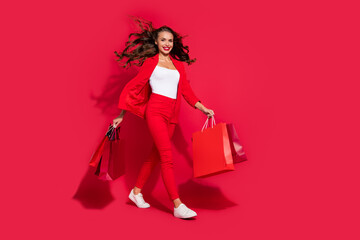 Photo of adorable stunning young woman wear suit jacket smiling walking holding bargains empty space isolated red color background