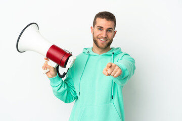 Young handsome caucasian man isolated on white background holding a megaphone and smiling while pointing to the front