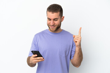 Young handsome caucasian man isolated on white background using mobile phone and lifting finger