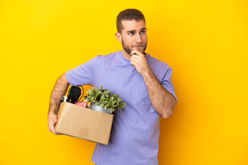 Young caucasian making a move while picking up a box full of things isolated on yellow background...