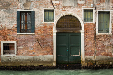 Fototapeta na wymiar Entrance in an old brick wall near water in Venice