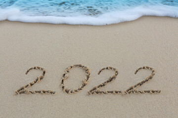 New Year 2022 written at the caribbean sand beach with sea wave .