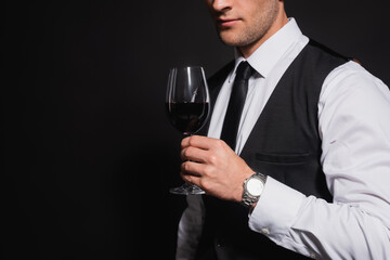 cropped view of elegant man holding glass of red wine isolated on black