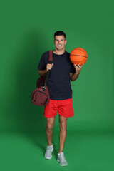Naklejka premium Handsome man with sports bag and basketball ball on green background