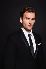 young confident man in elegant suit looking at camera on black